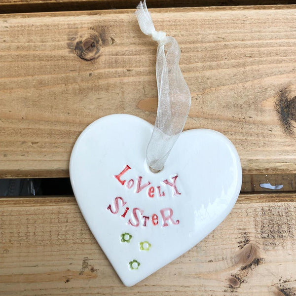 Hand painted ceramic heart featuring a flower design and the sentiment 'Lovely Sister'  Handmade in the UK using clay, glaze and paint sourced locally.  Material:  Ceramic