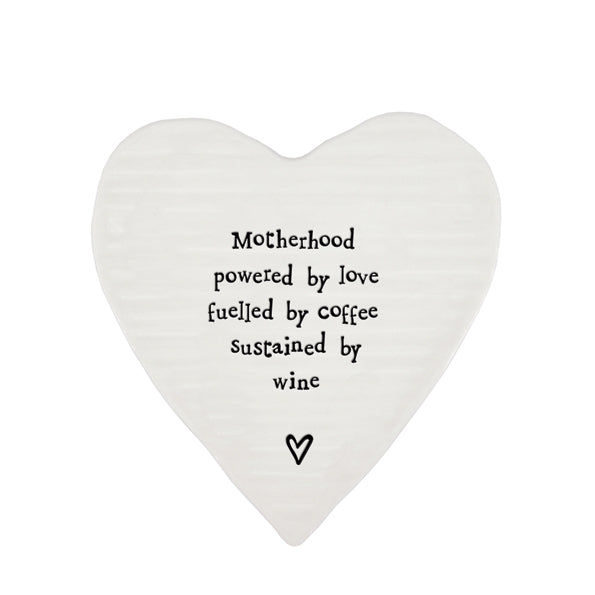 White porcelain heart shaped coaster with black text which reads Motherhood, powered by love, fuelled by coffee, sustained by wine