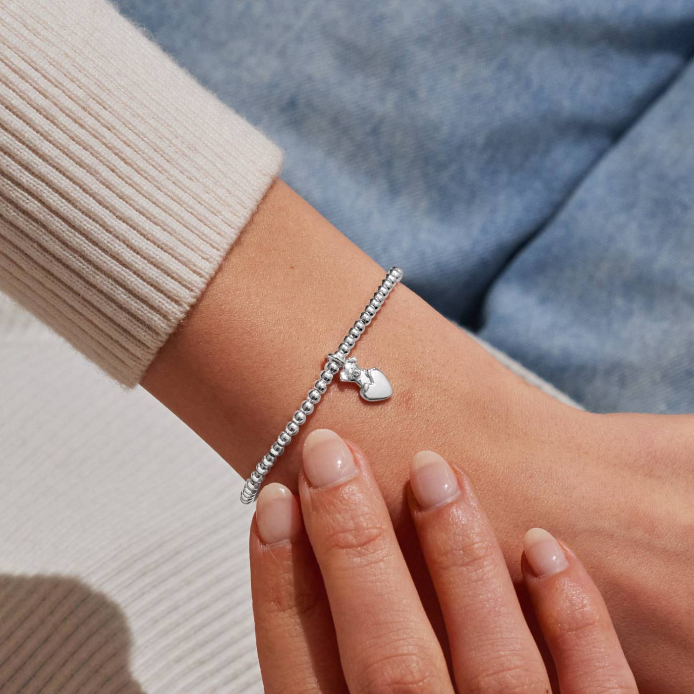 a woman's wrist wearing a silver beaded bracelet with a silver charm that features a dog sitting on a heart