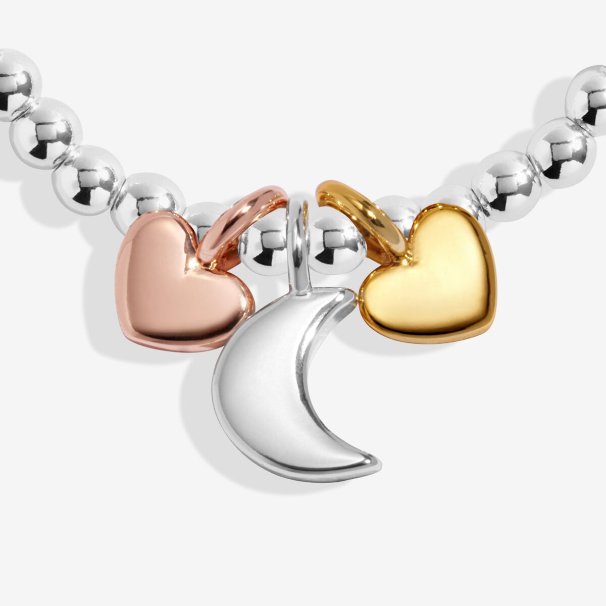 Silver plated beaded stretch Joma Jewellery bracelet with trio of charms - silver moon, gold and rose gold hearts. Presented on a sentiment card ready for gifting.