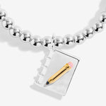 Joma jewellery girls stretch beaded bracelet with hanging book and pencil charm presented on a blush pink sentiment card.