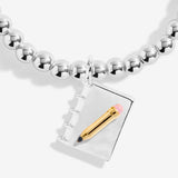 Joma jewellery girls stretch beaded bracelet with hanging book and pencil charm presented on a blush pink sentiment card.