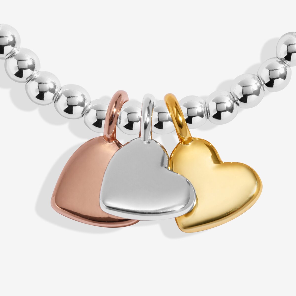 Joma jewellery stretch beaded bracelet with three solid hanging heart charms in silver, gold and rose gold plating presented on a foil stamped sentiment card.