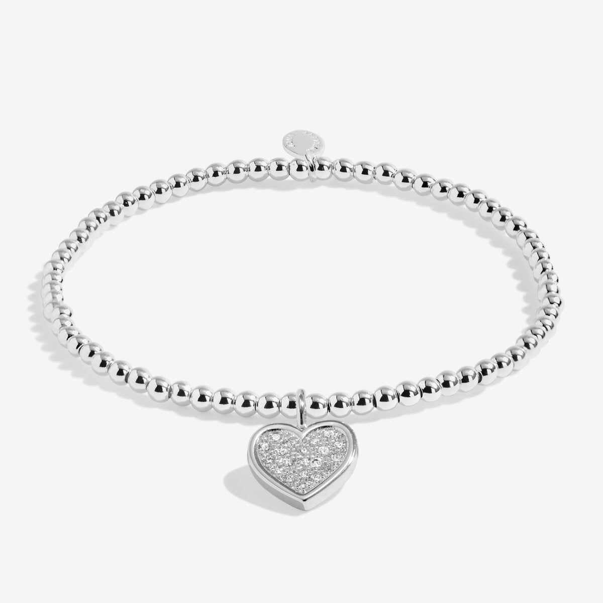 Silver plated girls Joma stretch bracelet with hanging heart charm presented on gifting card for Holy Communion