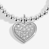 Silver plated girls Joma stretch bracelet with hanging heart charm presented on gifting card for Holy Communion
