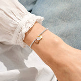 Bracelet with heart-shaped charms on a wrist, wearing a white lace sleeve.