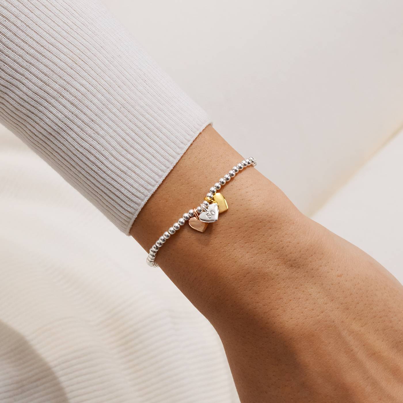 Bracelet with heart-shaped charms on a wrist against a neutral background