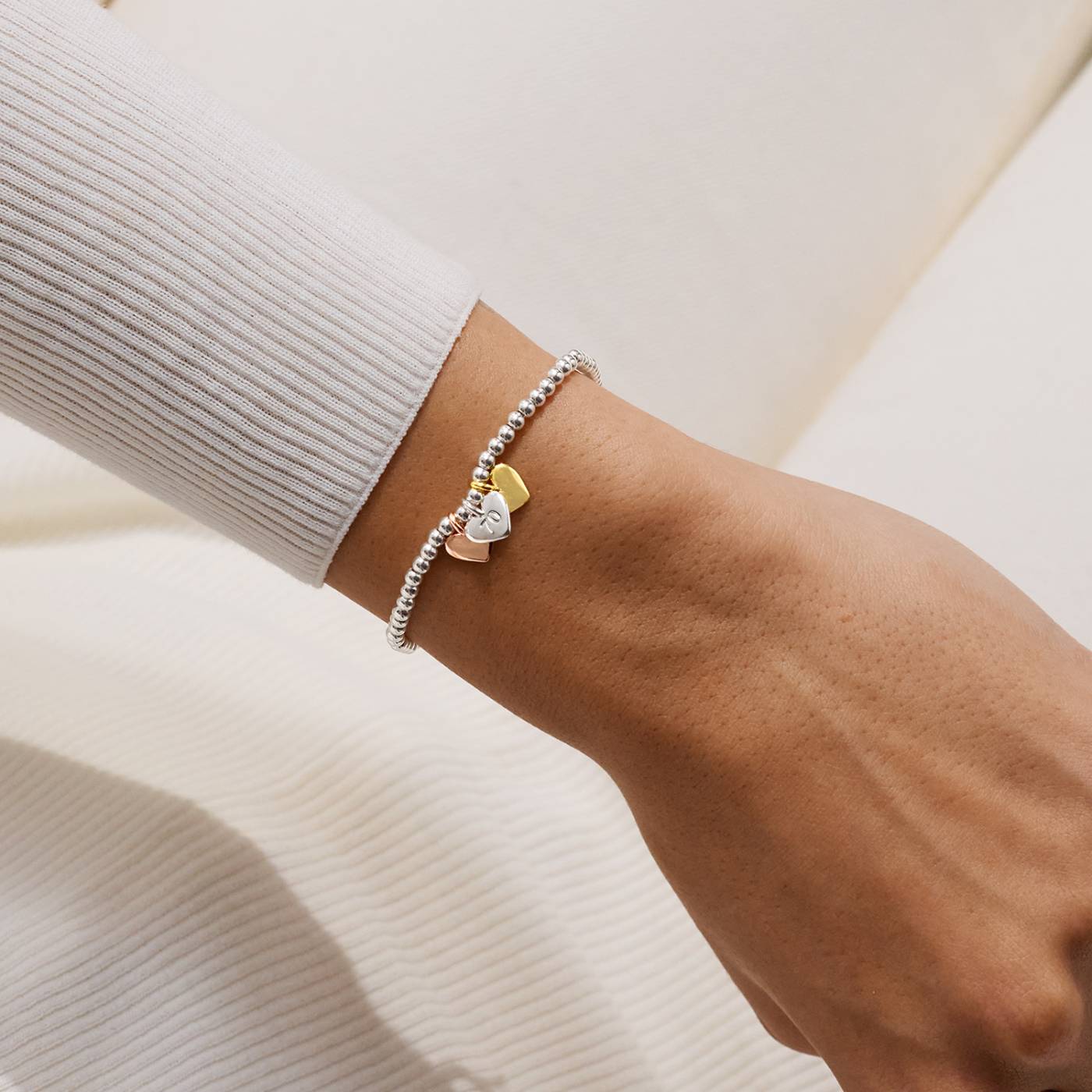 Close-up of a wrist wearing a bracelet with 3 heart-shaped charms on a neutral background