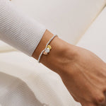 Close-up of a wrist wearing a bracelet with 3 heart-shaped charms on a neutral background