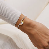 Close-up of a wrist wearing a bracelet with 3 heart-shaped charms on a neutral background