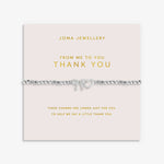 A silver beaded bracelet with heart charm and bow charm, presented on a pale pink card from Joma Jewellery that reads 'FROM ME TO YOU THANK YOU'.