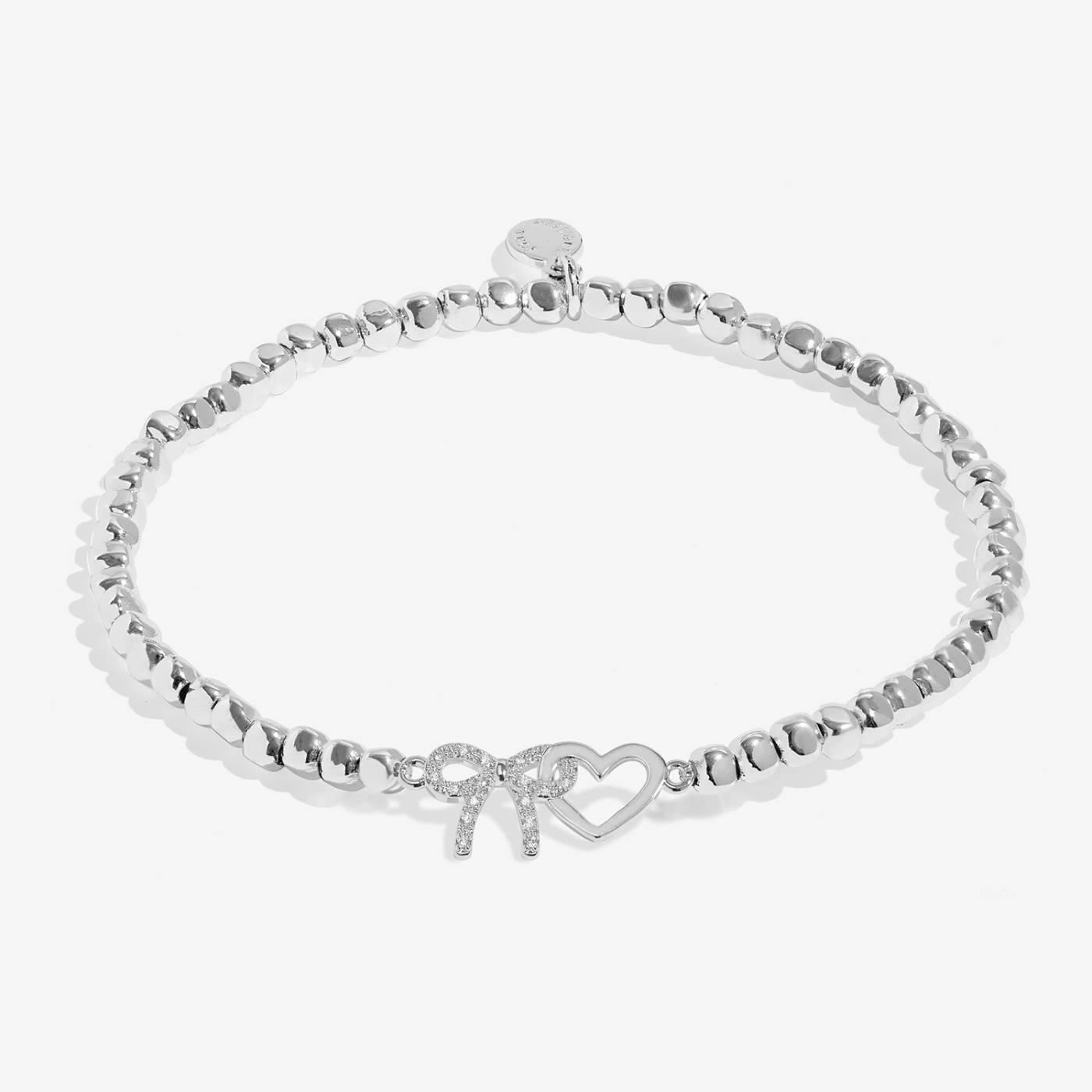 A silver beaded bracelet with a bow and open heart charm, embellished with small clear crystals, shown on a light grey background.