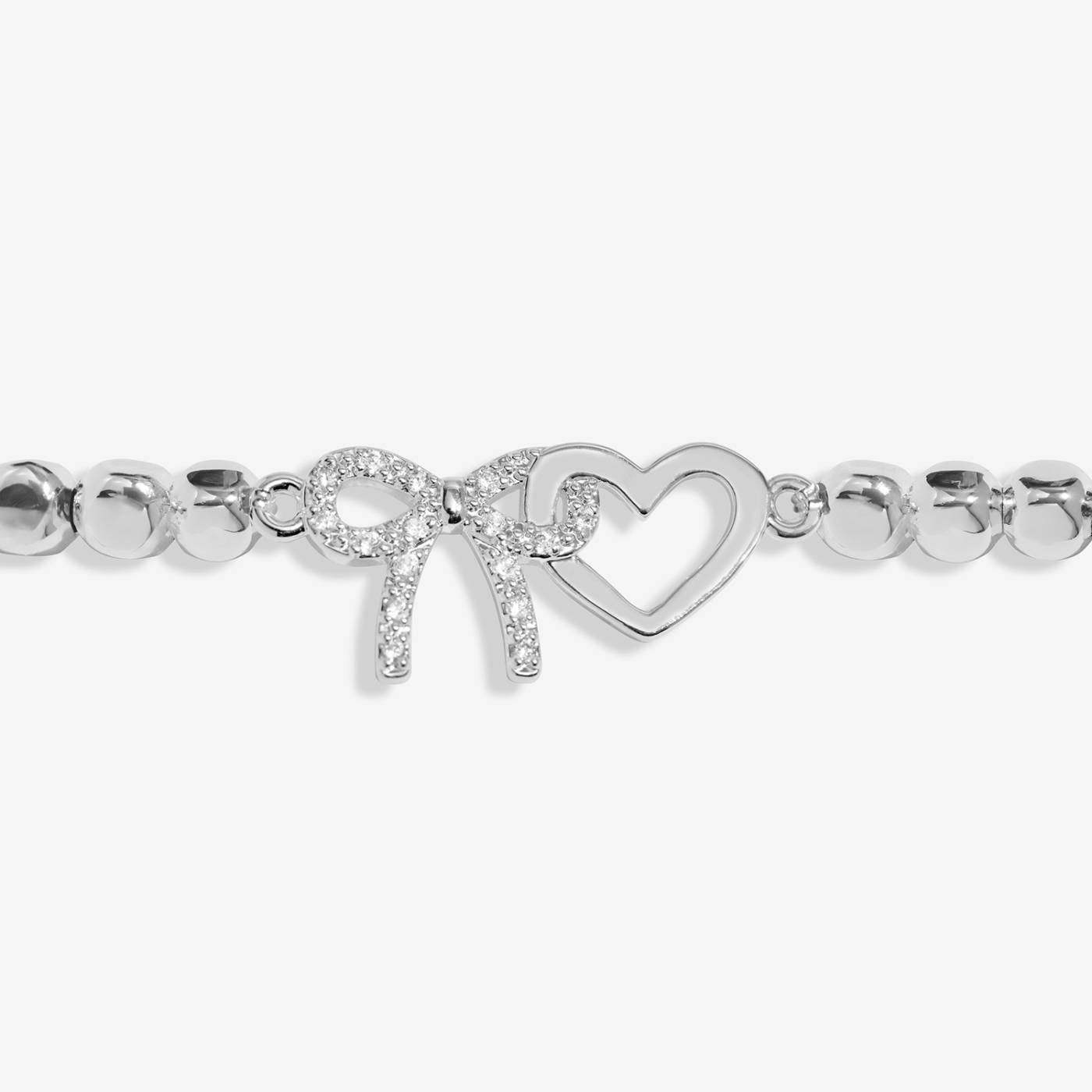 A silver beaded bracelet featuring a heart-shaped charm and a bow-shaped charm embellished with small clear stones, set against a light grey background.
