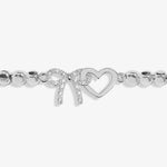 A silver beaded bracelet featuring a heart-shaped charm and a bow-shaped charm embellished with small clear stones, set against a light grey background.