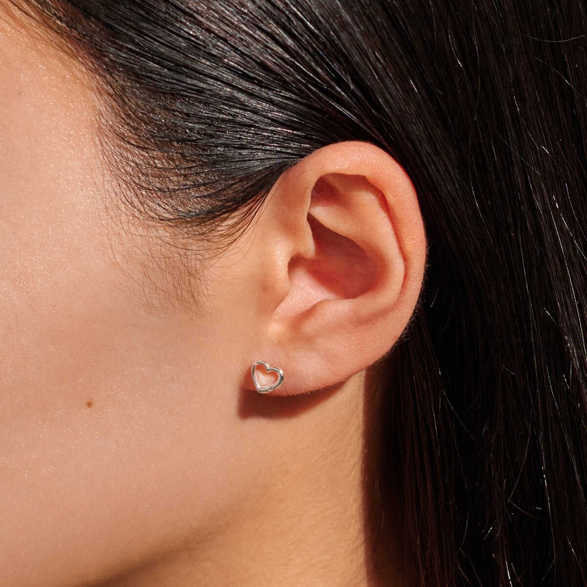 Close-up of an ear wearing a heart-shaped earring with dark hair in the background