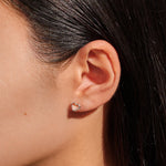 Close-up of an ear wearing a heart-shaped earring with dark hair in the background