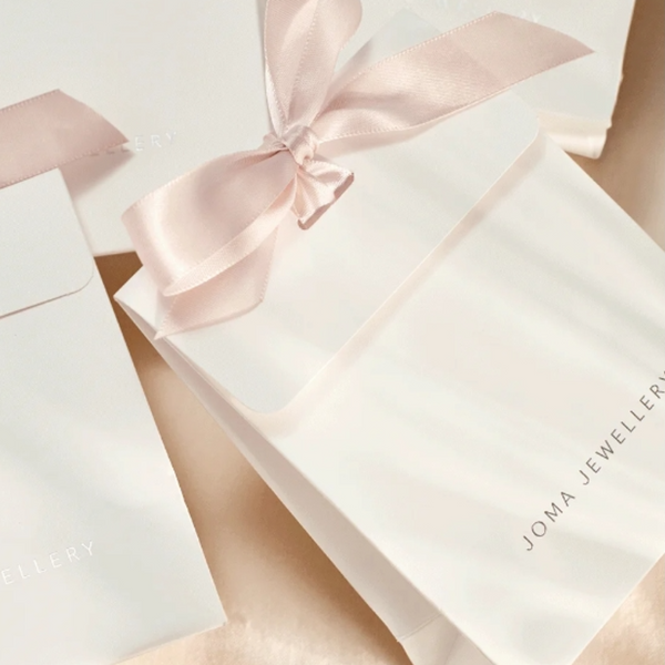 Joma Jewellery white envelope with pink ribbon for tying with Joma Jewellery in silver lettering on front.