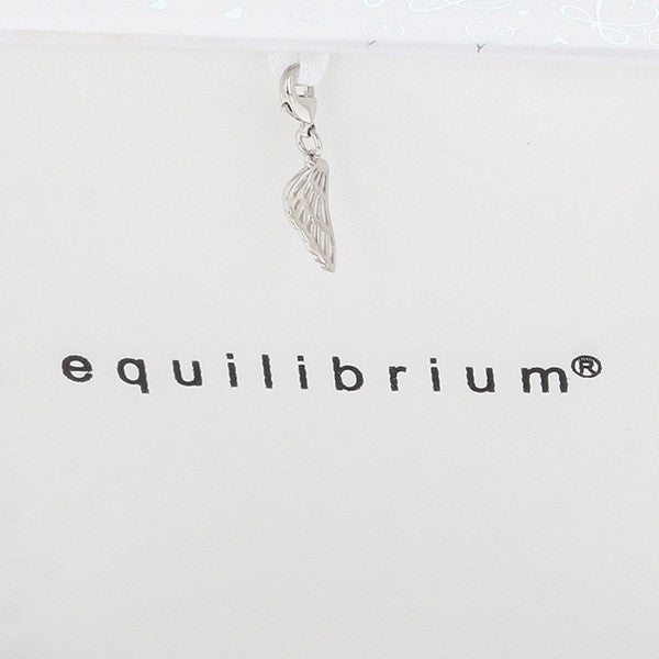 A silver wing-shaped pendant hanging from a white ribbon against a white background with the brand name 'equilibrium' printed below.