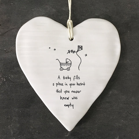 White Hanging Porcelain 'Wobbly' Round Heart baby gift from East of India which reads:  'A Baby fills a place in your heart that you never knew was empty.'  The heart features an engraved illustration in East of India's unique style.