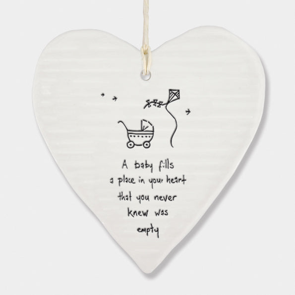 White Hanging Porcelain 'Wobbly' Round Heart baby gift from East of India which reads:  'A Baby fills a place in your heart that you never knew was empty.'  The heart features an engraved illustration in East of India's unique style.