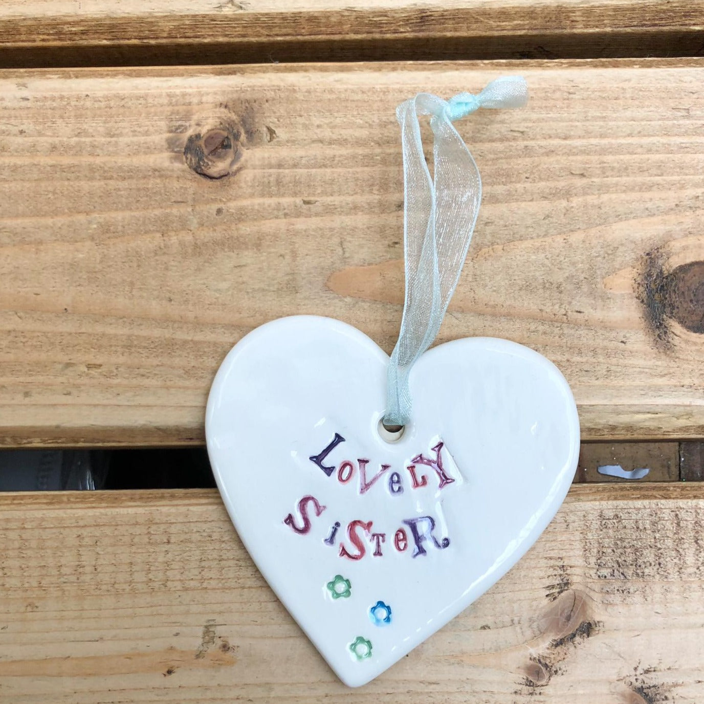 Hand painted ceramic heart featuring a flower design and the sentiment 'Lovely Sister'  Handmade in the UK using clay, glaze and paint sourced locally.  Material:  Ceramic