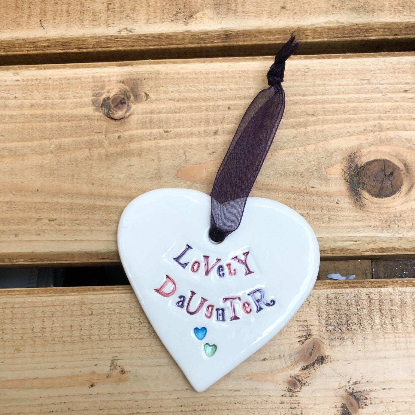 Hand painted ceramic heart featuring a flower design and the sentiment 'Lovely Daughter' Handmade in the UK using clay, glaze and paint sourced locally. Material: Ceramic