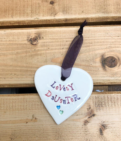 Hand painted ceramic heart featuring a flower design and the sentiment 'Lovely Daughter' Handmade in the UK using clay, glaze and paint sourced locally. Material: Ceramic