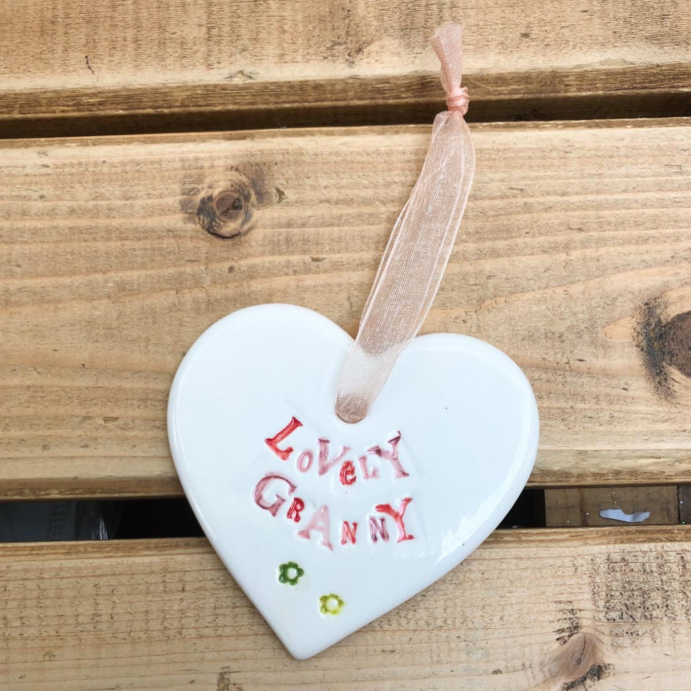 Hand painted ceramic heart featuring a flower design and the sentiment 'Lovely Granny' Handmade in the UK using clay, glaze and paint sourced locally. Material: Ceramic