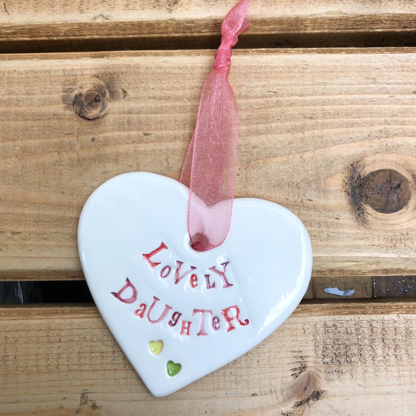 Hand painted ceramic heart featuring a flower design and the sentiment 'Lovely Daughter' Handmade in the UK using clay, glaze and paint sourced locally. Material: Ceramic