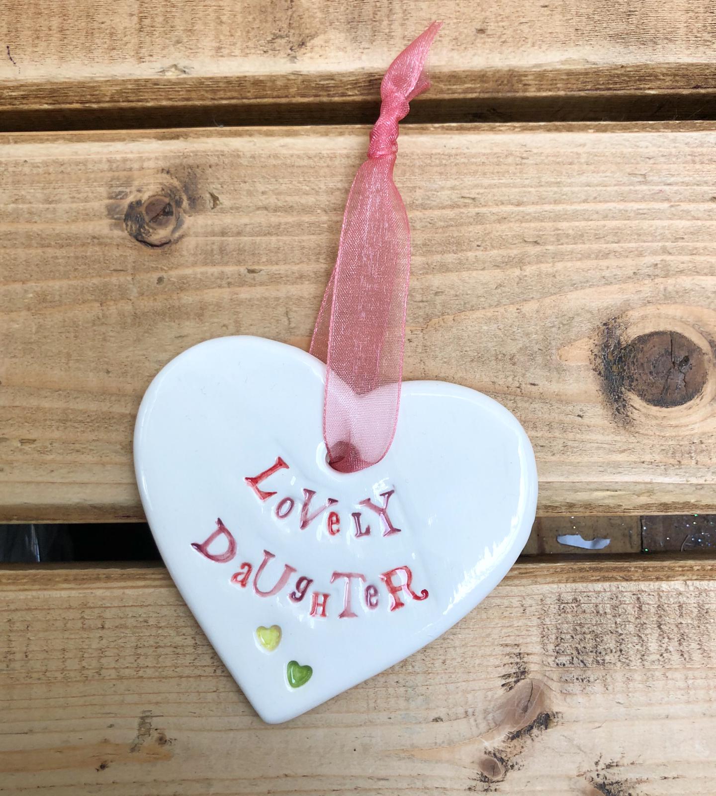 Hand painted ceramic heart featuring a flower design and the sentiment 'Lovely Daughter' Handmade in the UK using clay, glaze and paint sourced locally. Material: Ceramic
