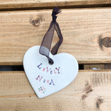 Hand painted ceramic heart featuring a flower design and the sentiment 'Lovely Nana'  Handmade in the UK using clay, glaze and paint sourced locally.  Material:  Ceramic