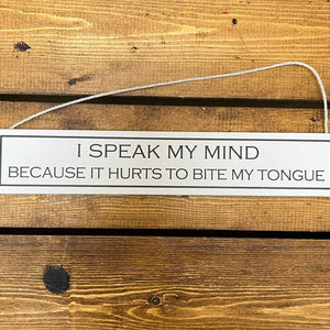 a rectangular wooden sign of neutral colour with black printed slogan that reads I speak my mind because it hurts to bite my tongue