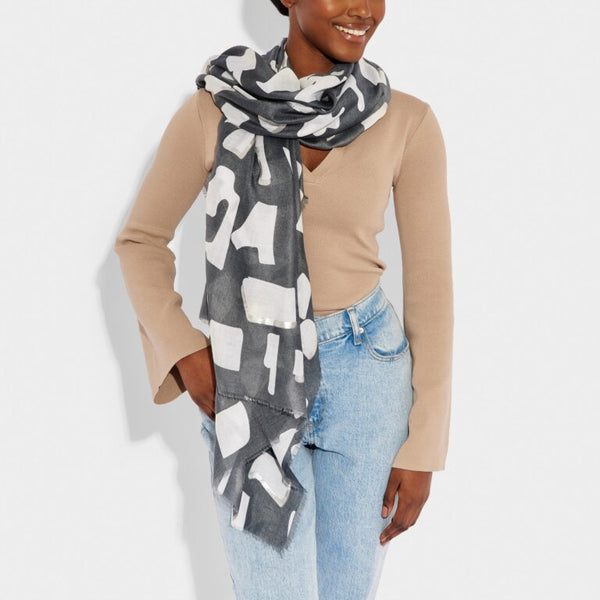 a smiling model in casual clothing wears a scarf in a light navy coloured abstract block print design